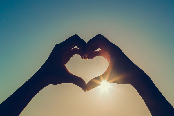 Silhouette of hands making a heart shape on a blue gradient background