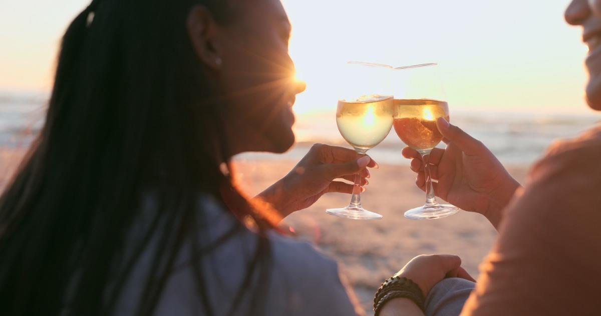 a couple sitting on the beach watching the sunset with a glass of champagne.